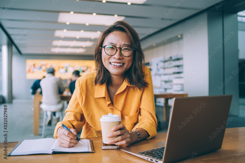 Portrait of happy Asian woman smiling at camera during studying process in university campus feeling excited from exam preparation, emotional female in trendy spectacles e learning in coffee shop Portrait of happy Asian woman smiling at camera during studying process in university campus feeling excited from exam preparation, emotional female in trendy spectacles e learning in coffee shop