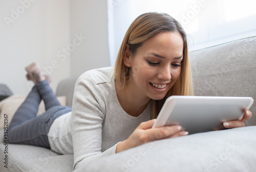 Woman using tablet on a home couch. Woman surfing on line or working from home concept