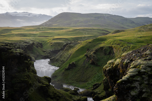 Beautiful smooth river in Iceland surrounded by green hills during the sunset on the Fimmvorduhals hiking trail close to Skogar