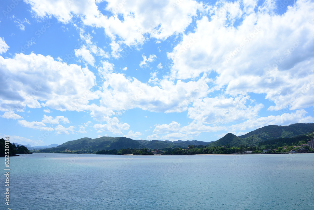 Vista de tierra desde el mar con un gran cielo azul lleno de nubes blancas