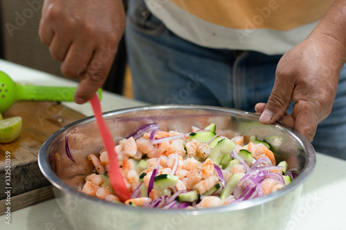 Mexican seafood made with shrimps and vegetables in a bowl is being prepared by an unrecognizable person