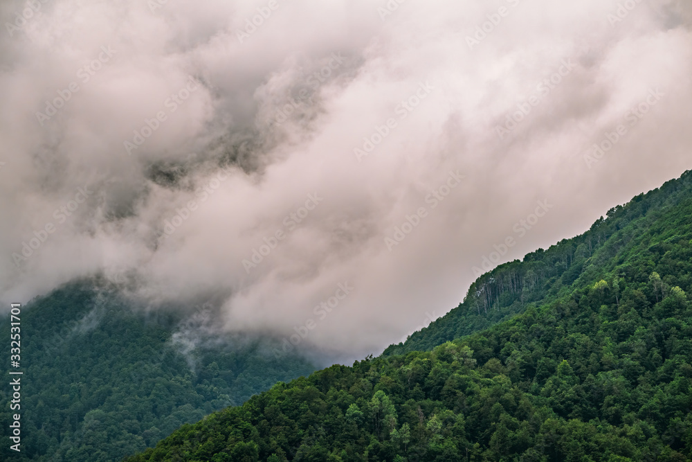 High mountain with green slopes hidden in clouds and fog.