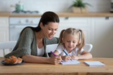 Loving young mother and little preschooler daughter sit at table drawing on paper together, caring mum or nanny playing with small girl child, paint pictures in notebook, early development concept
