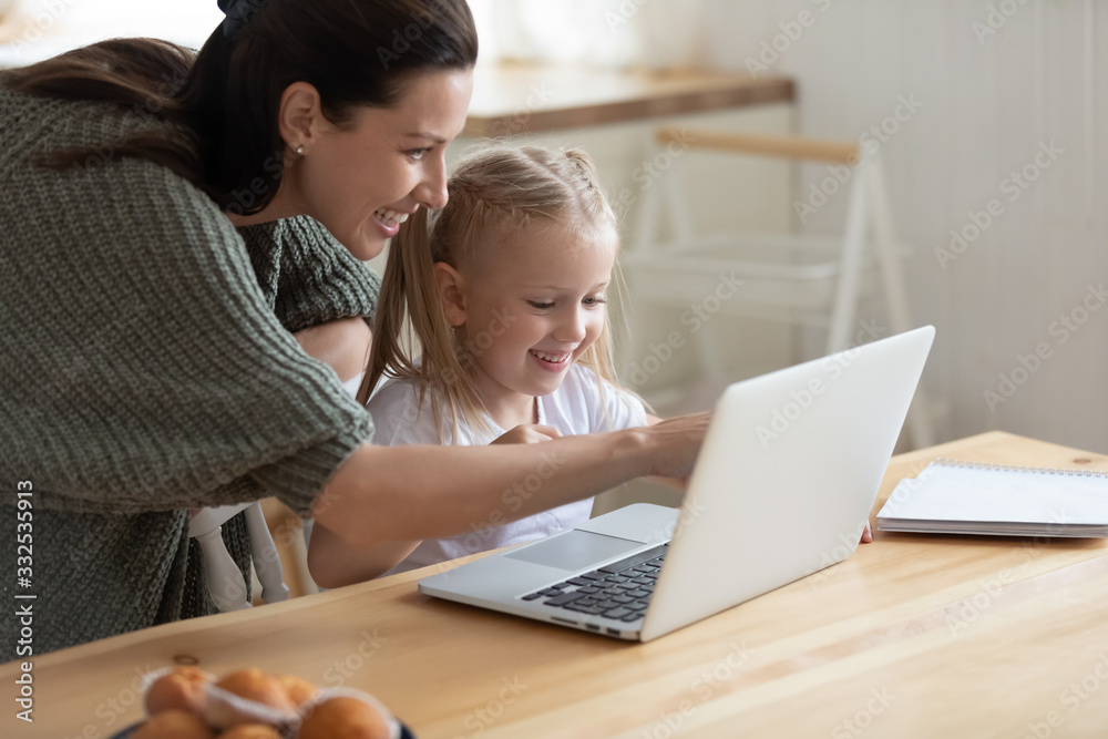 Happy young mother and cute preschooler daughter watch funny video on  laptop together, smiling mom or nanny and little girl child have fun  playing game on computer or studying learning online Stock
