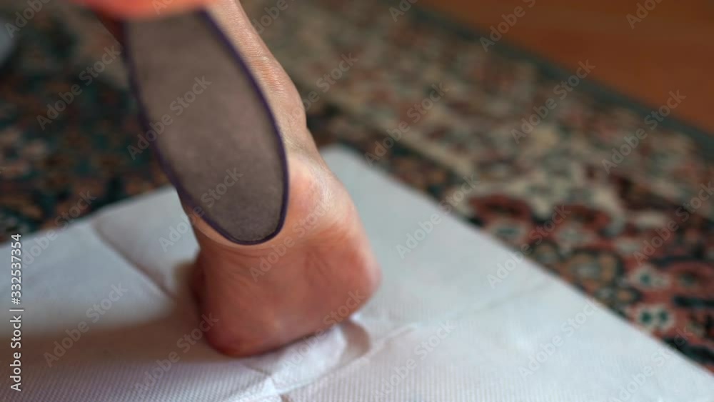 Close-up of woman's hand holding peeling brush and removing old dry skin from foot heel, removing callus with grinding treatment at home Close-up of woman's hand holding peeling brush and removing old dry skin from foot heel, removing callus with grinding treatment at home