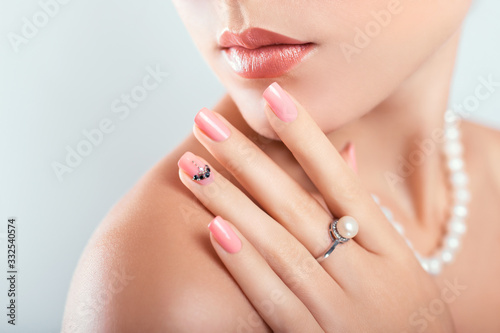 Nail art and design. Beautiful woman wearing make-up and pearl jewellery showing pink manicure with gems