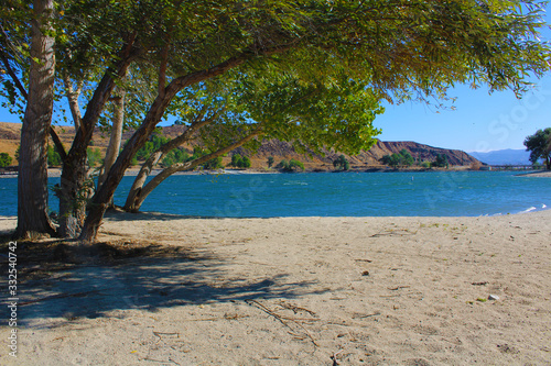 a stunning shot of the vast blue lake water surrounded by lush green trees with mountain ranges and blue sky at Castaic Lake in California USA photo