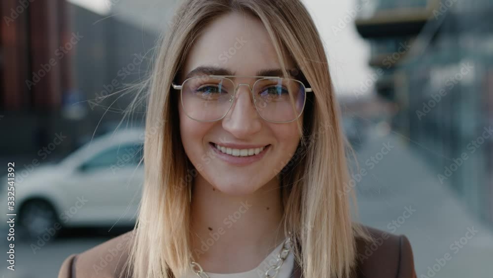 Extrime close up view of blonde caucasian young happy woman in glasses looking to the camera and smiling in the city spring sunlight outdoor successful female Extrime close up view of blonde caucasian young happy woman in glasses looking to the camera and smiling in the city spring sunlight outdoor successful female