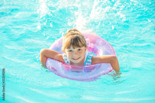 Little girl lying in swimming pool learning to swim on inflatable circle. Summer holidays, heat and water