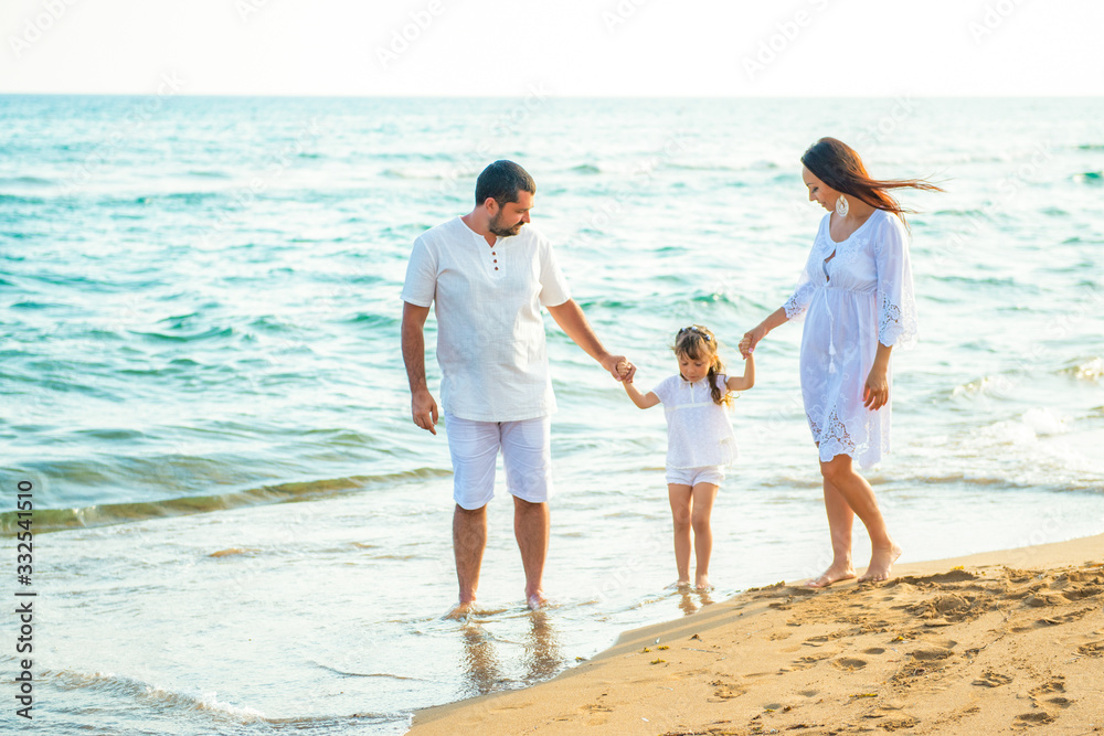 Happy family mom, dad and little daughter walk along the coast on sea beach at resort