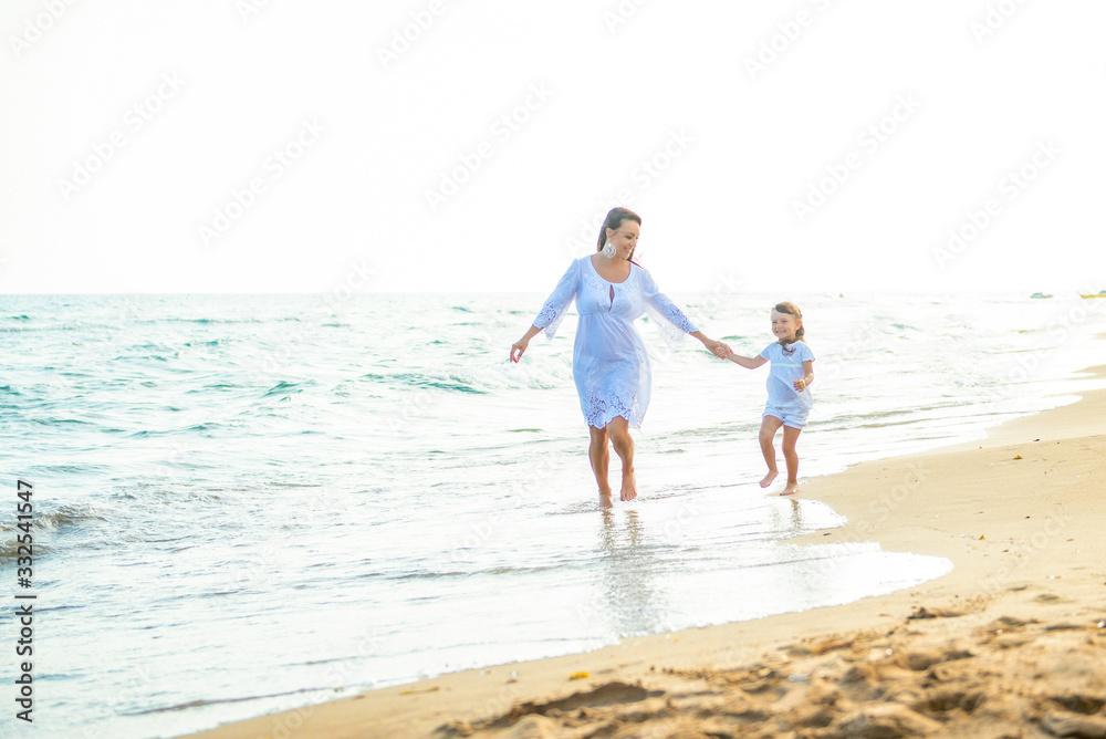 Happy family mom and little daughter run walk along the coast on sea beach at resort