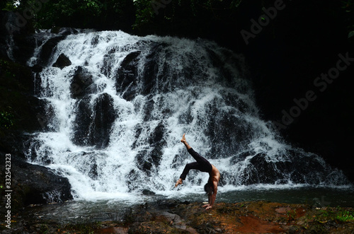 A movement artist doing a handstand in front of a waterfall