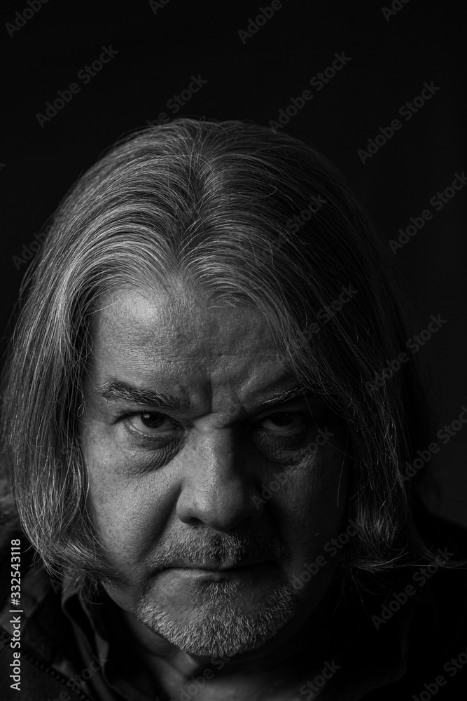 Studio extreme closeup head shot of man. He is serious and looking to the camera. He has long hair. This is a black and white image with the skin highly textured. Studio extreme closeup head shot of man. He is serious and looking to the camera. He has long hair. This is a black and white image with the skin highly textured.