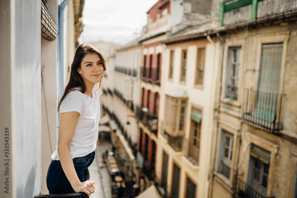 Young european woman spending free time home.Self care,staying home.Enjoying view on the balcony.Relaxing at home.Hotel room balcony view,vacation in Europe.Narrow street in Granada,Andalucia,Spain.