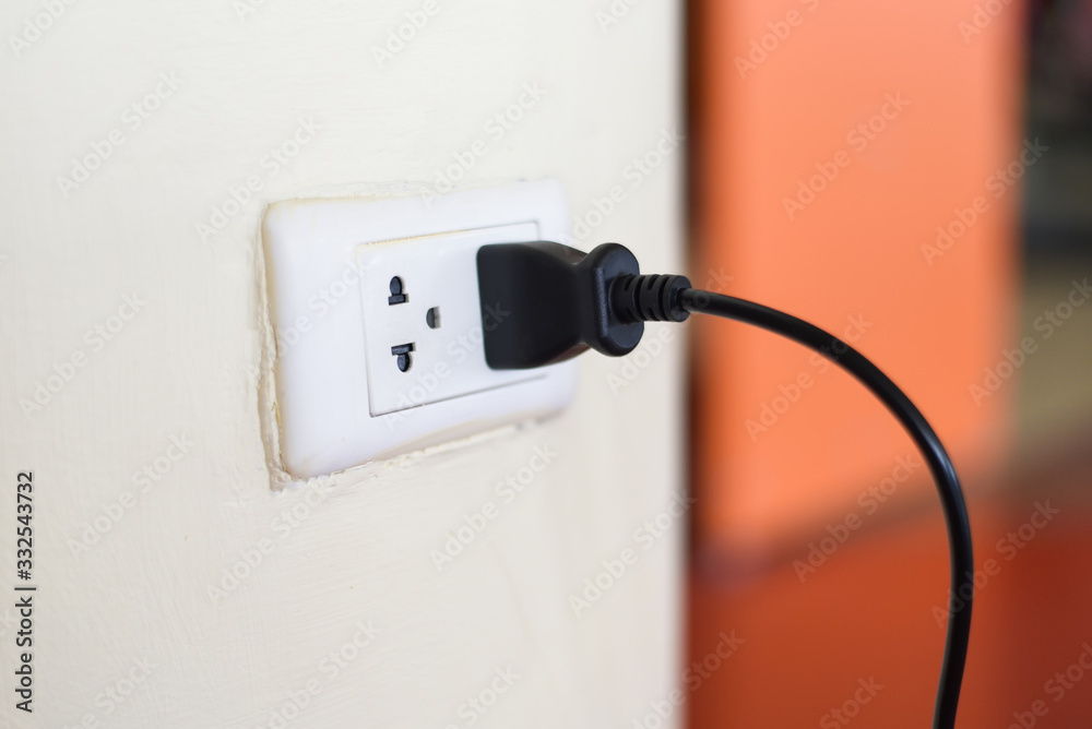 Home outlet plug is plugging socket on wall with black power cord cable - Power plug connecting electrical plug