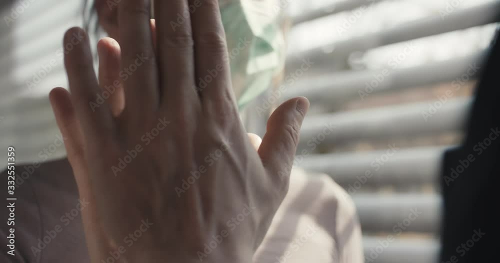 Woman with protective face mask behind protective glass touches and kisses her boyfriend during coronavirus pandemic isolatied in hospital quarantine