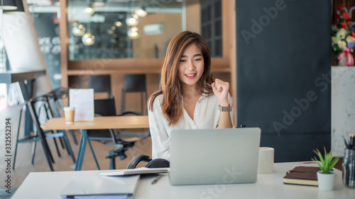 Happy young asian businesswoman sitting on her workplace in the office. Young woman working at laptop in the office.