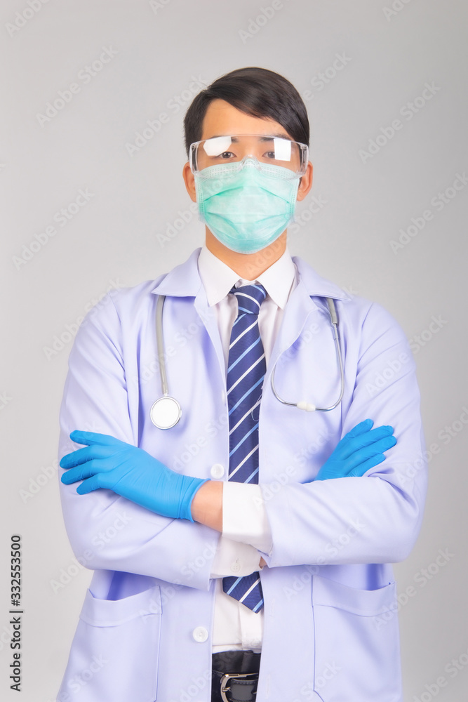 Medical doctor in white uniform doctor wears medical gloves, medical masks and and wearing protective glasses with crossed arms look at camera on gray background, corona virus concept, covid19 concept Medical doctor in white uniform doctor wears medical gloves, medical masks and and wearing protective glasses with crossed arms look at camera on gray background, corona virus concept, covid19 concept