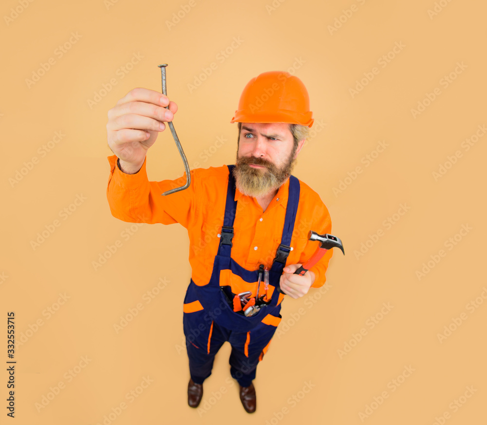 Curve nail. Worker holds curve nail. Builder in construction helmet. Repairment tools. Hard hat. Hammer. Nails. Industrial worker. Repair. Building. Industry. Technology. Bearded builder.
