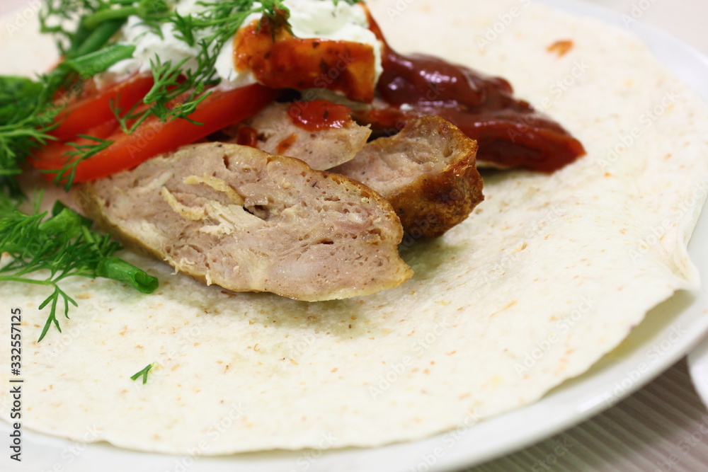 Hot lula kebab with tomato sauce with fresh vegetables and herbs on a tortilla or pita bread on a plate