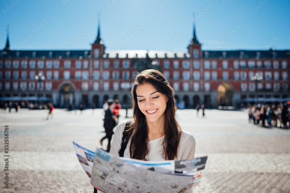 Visiting famous landmarks and places.Cheerful female traveler at famous Plaza Mayor square reading a map. Marid,Spain travel experience.