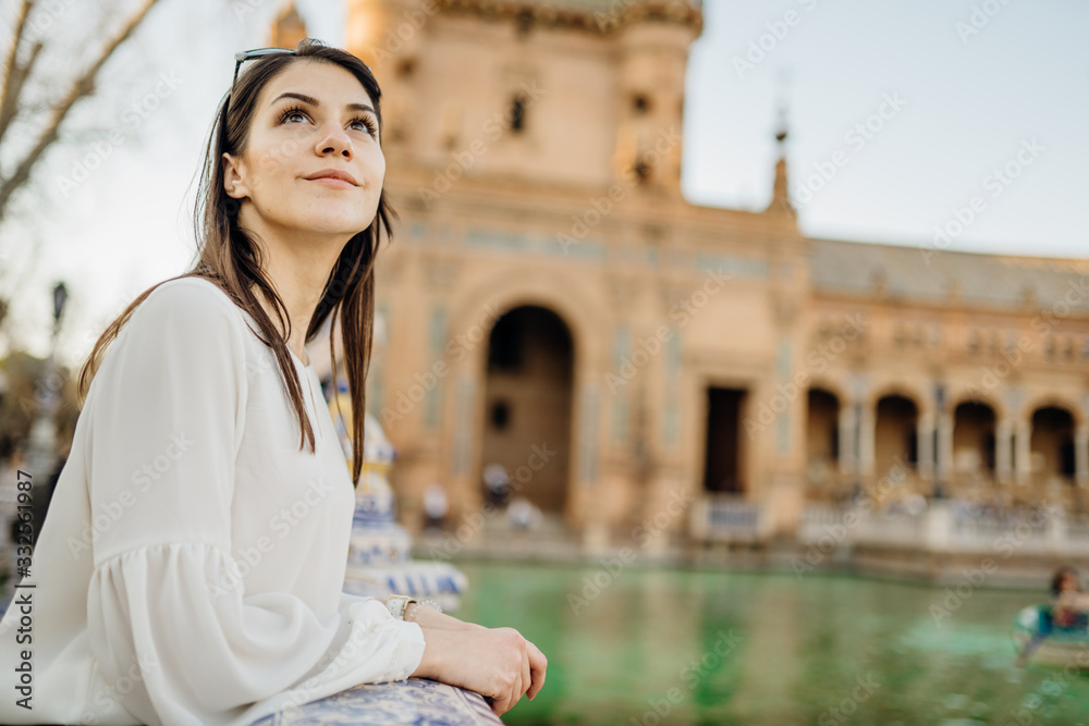 Enjoying beautiful historical landmark.Young tourist woman looking over Plaza de Espana in Seville,Andalusia,Spain.Traveling to Spain.Sunset on Spain Square.Pensive woman in public square in Europe.