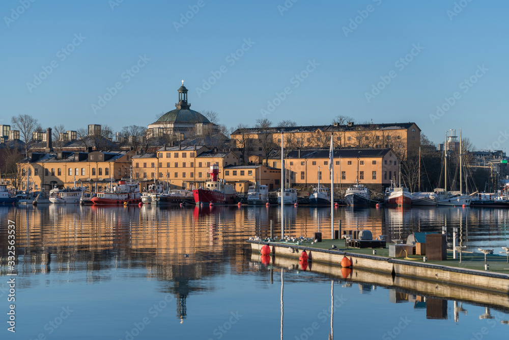 Harbor view over the old town district Gamla Stan, the islands Skeppsholmen and Blasieholmen with boats and piers in an early sunny tranquil spring day