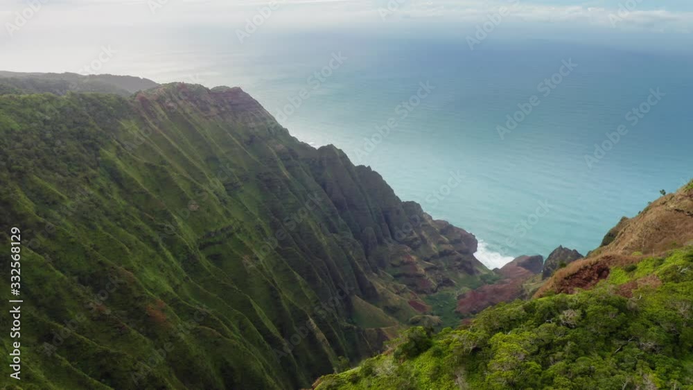 Na Pali Coast State park. Tropical nature. Aerial footage over deep picturesque gorge on Hawaiian coast. Ribbed grassy slopes stretch down to the bottom. Calm blue ocean is seen at the background.4K Na Pali Coast State park. Tropical nature. Aerial footage over deep picturesque gorge on Hawaiian coast. Ribbed grassy slopes stretch down to the bottom. Calm blue ocean is seen at the background.4K