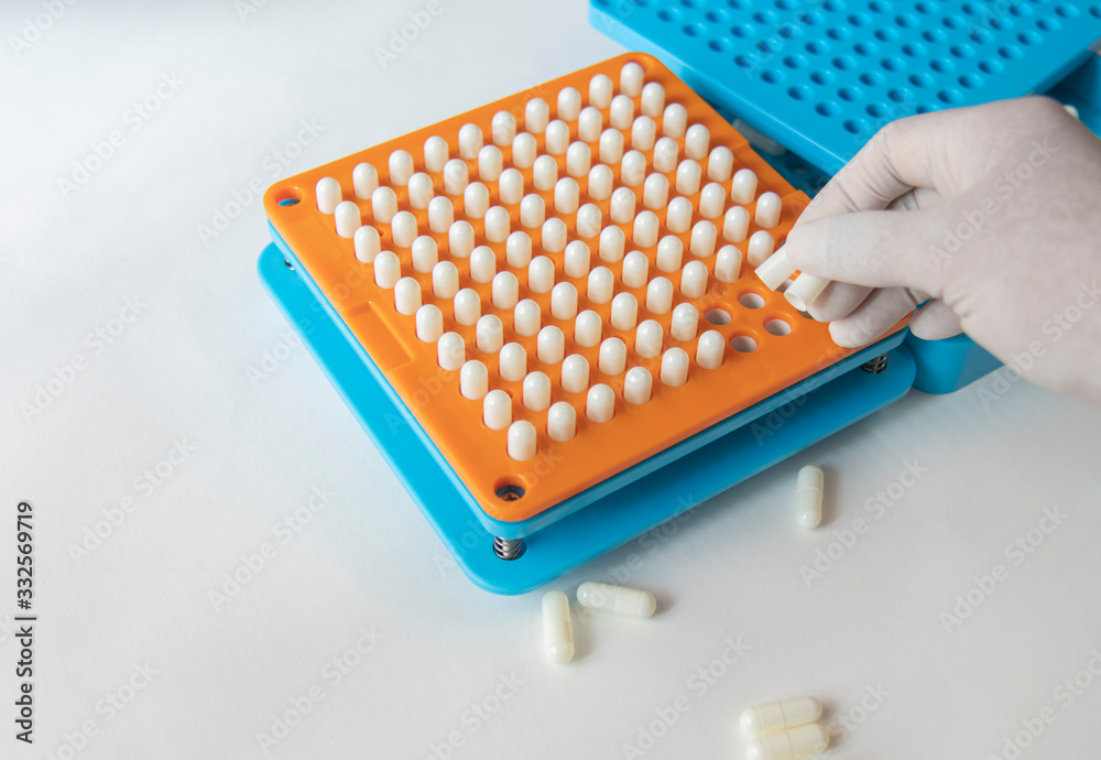 White pill capsules are row in orange filling machines hold by hand White pill capsules are row in orange filling machines hold by hand