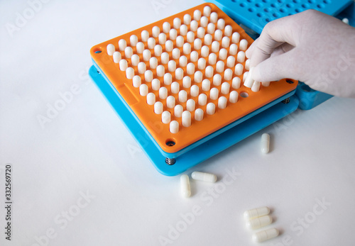 White pill capsules are row in orange filling machines hold by hand