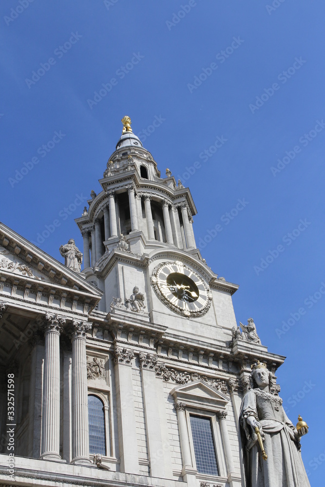 Fototapeta premium Clock tower and statue of Queen Anne at St Paul's Cathedral against blue clear sky, London, UK