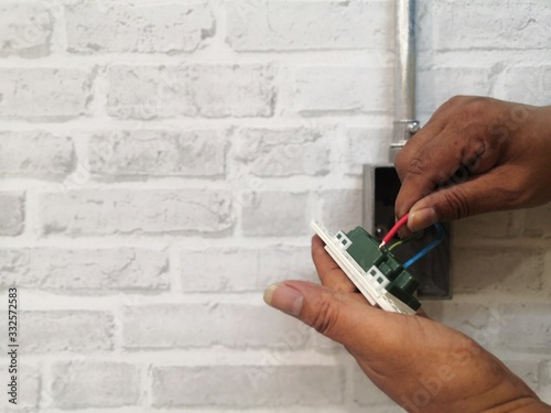 Foto Electrician installing wall socket for electrical system work on gray brick wall