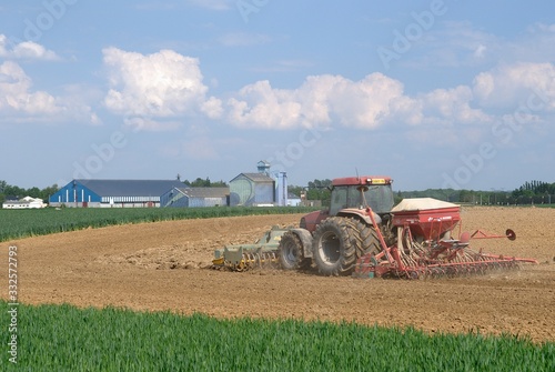 Semis mais avec semoir 32 rangs de 4m et outil ottavioli (tasseligne) à l'avant. Coopérative agricole en arrière plan photo