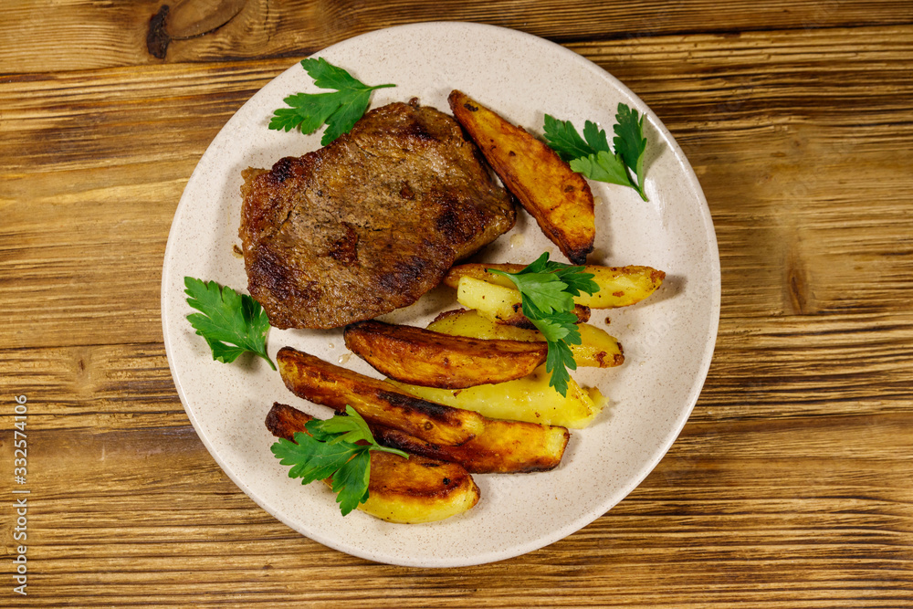 Fried beef steak with potato wedges on wooden table. Top view