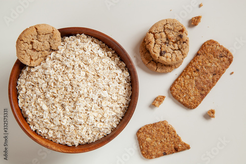 Dry oatmeal in a round wooden plate and oatmeal cookies on the table.