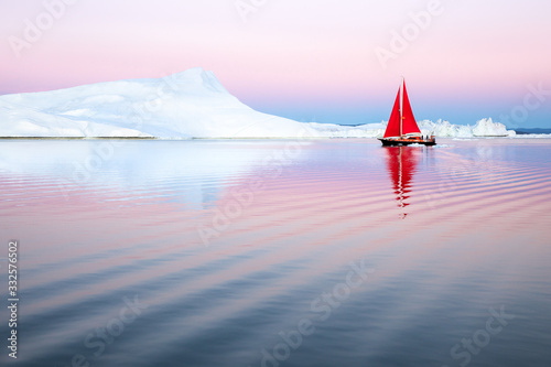 Sail boat with red sails cruising among ice bergs after sunset. Disko Bay, Greenland. photo