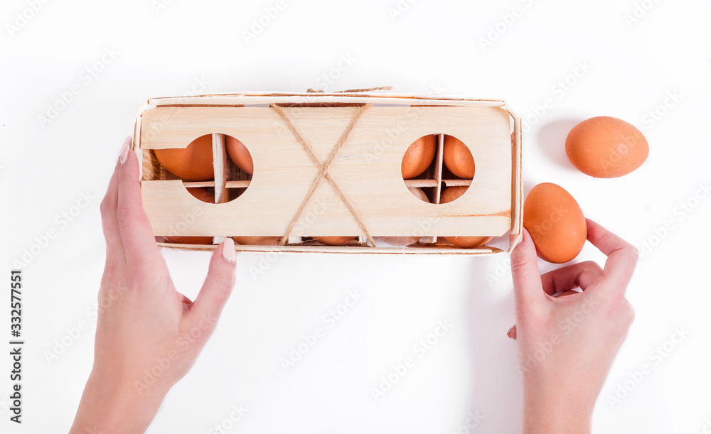 Fototapeta premium Female hands hold 10 natural fresh brown eggs in eco-friendly wooden packaging
