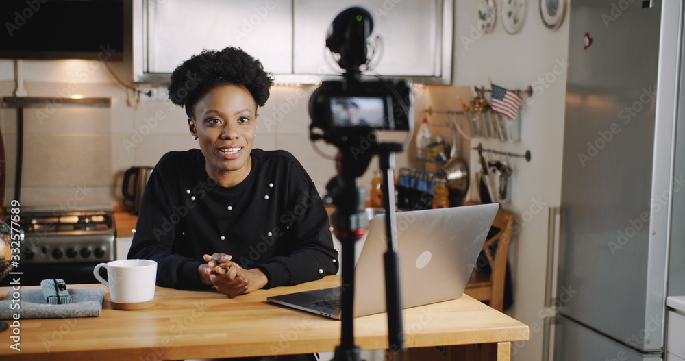 Happy smiling young beautiful black vlogger woman filming new video using professional camera at home table slow motion. Happy smiling young beautiful black vlogger woman filming new video using professional camera at home table slow motion.