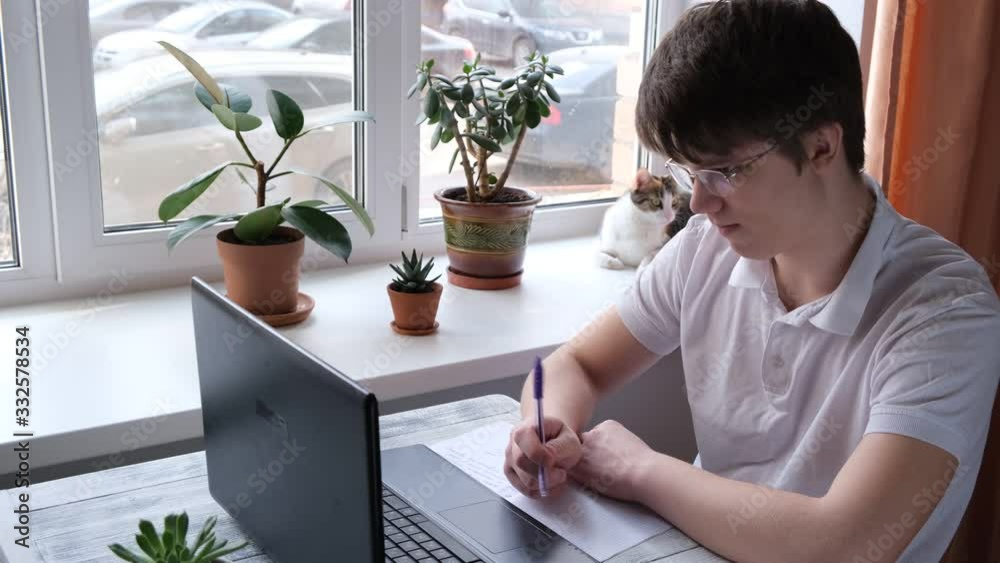 Young man studying at home using laptop. Home school, online education, home education, quarantine concept. 4k footage.