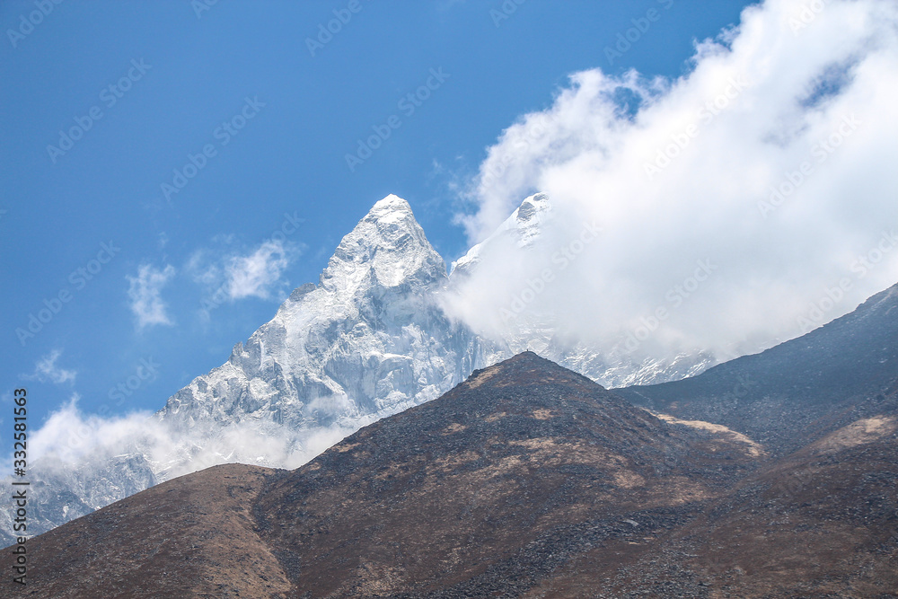 View of white snowy Ama Dablam mountain peak in Himalayas during the day on the way to Everest base camp in Nepal. Clouds on the sky. Theme of beautiful mountain landscapes.