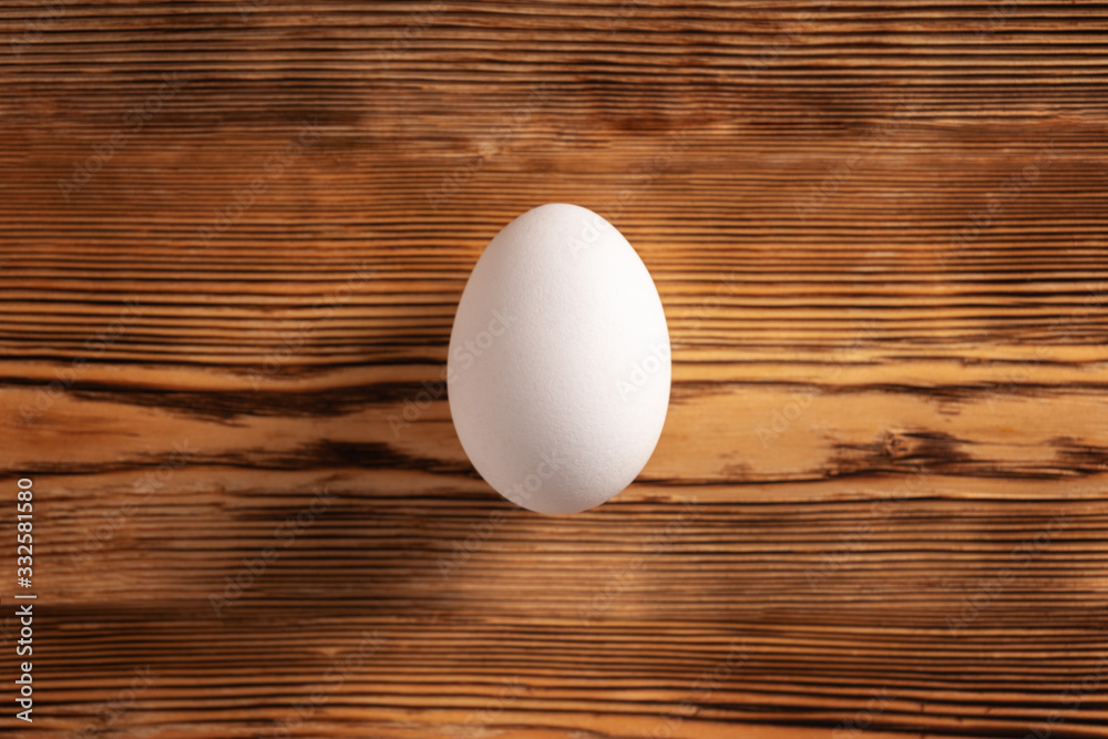 One white egg is centered on a wooden table. The view from the top. One white egg is centered on a wooden table. The view from the top.