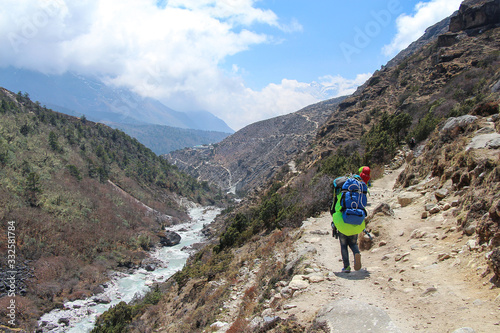 Back view. Some nepalese sherpa porters with backpacks walks on footpath in Himalayas on the way back from Everest base camp. Imja Khola river flows near footpath. Theme of trekking in Nepal. photo