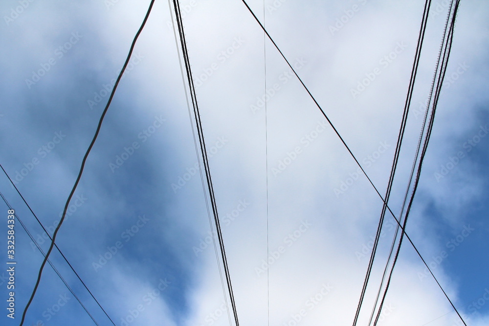 Interweaving of wires and cables against the blue sky with clouds. Industrial city landscape Interweaving of wires and cables against the blue sky with clouds. Industrial city landscape