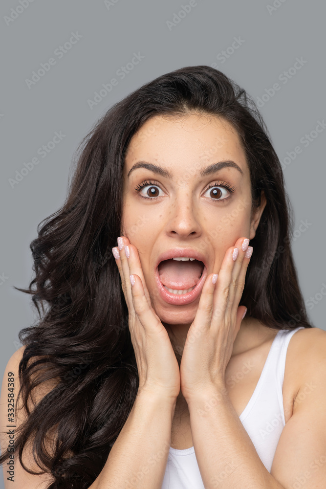 Pretty brunette girl touching her face and looking shocked Pretty brunette girl touching her face and looking shocked