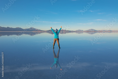 Sunrise on Salar de Uyuni in Bolivia covered with water, woman tourist on salt flat desert and sky reflections