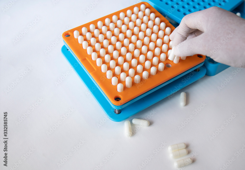 White pill capsules are row in orange filling machines hold by hand White pill capsules are row in orange filling machines hold by hand