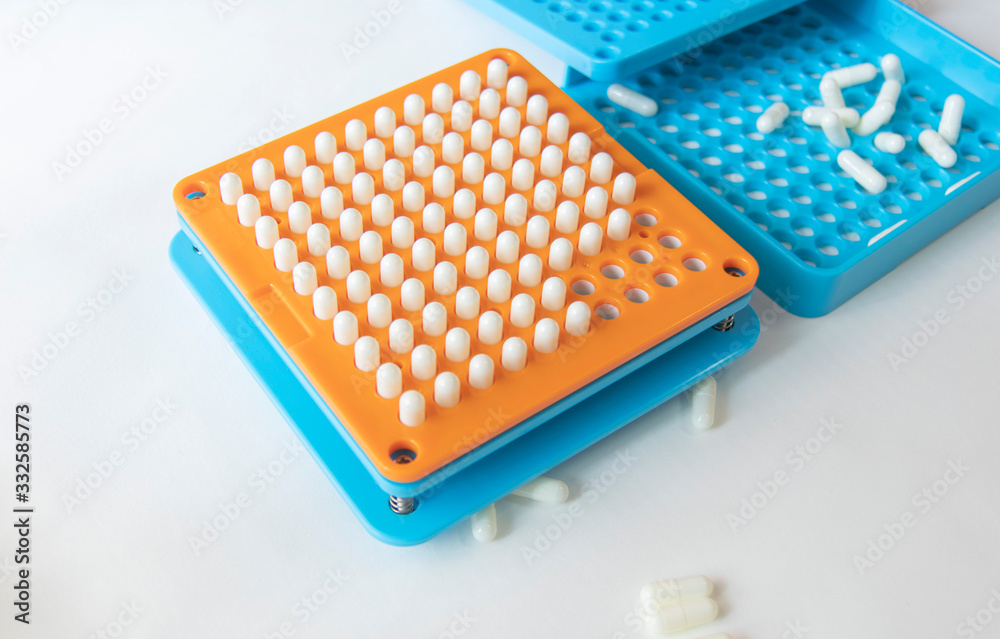 White pill capsules are row in orange filling machines hold by hand White pill capsules are row in orange filling machines hold by hand