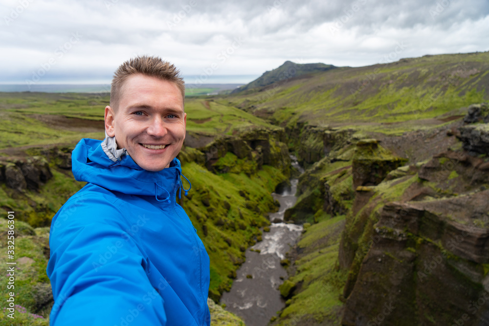 Naklejka premium Young smiling man with river and green canyon on background takes a Selfie. Concept of freedom movement and freedom