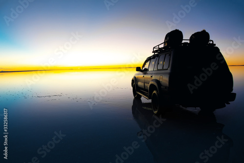 Sunrise on Salar de Uyuni in Bolivia covered with water, car in salt flat desert and sky reflections