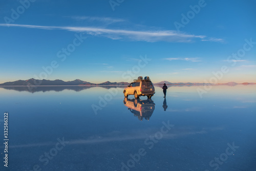 Sunrise on Salar de Uyuni in Bolivia covered with water  car and man in salt flat desert and sky reflections